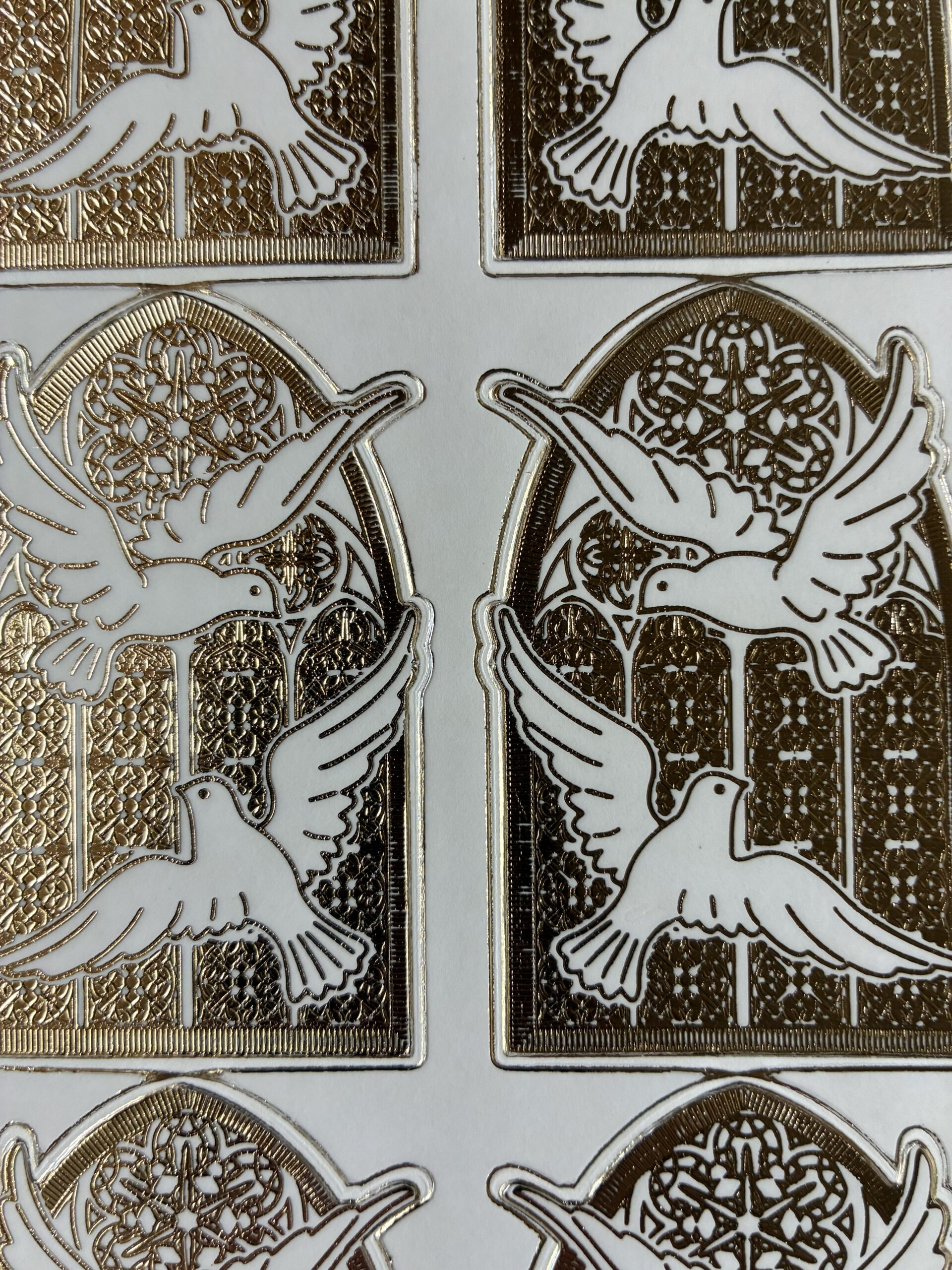 Doves Window Transparent Gold. Religious themed peel off stickers with 6 images of a pair of doves in front of a stained glass window in a gold colour.